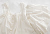 A white vintage blouse with lace trim and buttons, laid flat on a white surface.