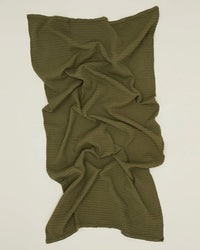 The Hawkins New York Simple Waffle Bath Sheet in Olive, featuring a textured waffle weave, is laid flat and loosely crumpled on a neutral background.