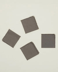 The Essential Cocktail Napkins in Dark Grey by Hawkins New York are a set of four 100% cotton napkins with frayed edges, shown loosely arranged on a light background.