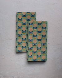Set of four Kesya Table Napkins in Sage by Soil to Studio, featuring a repeating blue, yellow, and beige thistle flower print on a light green background—perfect for adding handmade charm to your table decor.