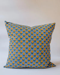The Pakhi Linen Pillow by Soil to Studio is a 22 x 22 in square cushion cover in Palace Blue, adorned with a repeating yellow and orange floral motif on a plain light background.