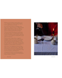 A spread from "A Meal For Two" by Chronicle Books shows text on the left and, on the right, a photo of two people—one in red, one in dark clothing—enjoying an intimate candlelit dinner set with plates, glasses, and a candle.
