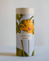 A cylindrical container labeled Chamomile Tea Gift Set by The Quiet Botanist, adorned with yellow chamomile flowers and green leaves on a light background—ideal for enjoying a soothing loose leaf herbal infusion.