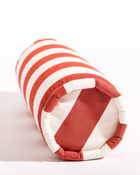 The Bolster Pillow - Crew Le Sirenuse Stripe by Business & Pleasure Co features red and white diagonal stripes, is spill, stain, and fade resistant, and rests on its side against a white background—ideal for indoor or outdoor use.