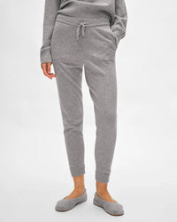 A person wearing the White + Warren Cashmere Jogger in Grey Heather, paired with a matching long-sleeve top and gray slippers, stands against a plain white background with one hand in their pocket.