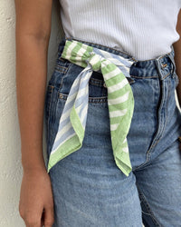 Wearing high-waisted blue jeans and a white ribbed tank top, this look features the Casa Amarosa Stripe Hand Block Printed Scarf in Green & Blue styled as a belted bow at the waist.