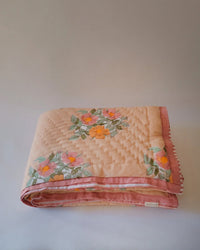 The Dia Hand Block-printed Reversible Quilt - Throw by Soil to Studio, shown folded against a plain background, features hand-quilted cotton with a light pink base and embroidered orange and pink flowers with green leaves.