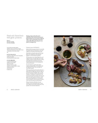 A tabletop scene showcases A Meal For Two by Chronicle Books: sliced steak, roasted garlic potatoes, and chimichurri sauce on a large tray. Hands serve plates amid drinks, cutlery, a candle, and an easy weekday meal recipe on the left.