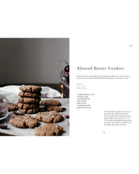 A stack of almond butter cookies sits on a white tablecloth with cherries in a glass, showcasing a tasty breakfast idea from "Wonderful Morning - Recipes For A Delicious Start To the Day" by Cozy Publishing.