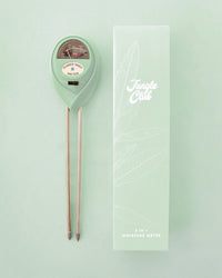 A Jungle Club 3-in-1 Moisture Meter in Lagoon with metal probes is displayed next to its light green branded box, both set against a pastel green background.