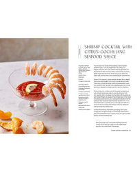 A glass dish with shrimp, seafood sauce, and lemon sits beside orange chips on marble—a perfect self-care meal inspired by "Snacking Dinners" from Chronicle Books. Recipe text appears on the left.