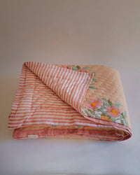 The Dia Hand Block-printed Reversible Quilt - Throw by Soil to Studio features pink and white stripes on one side and a floral print with pink flowers and green leaves on the other, set against a plain background.