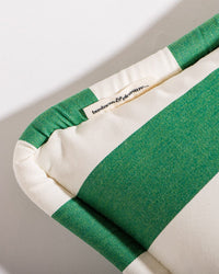A close-up of the Business & Pleasure Co Small Square Throw Pillow - Crew Canyon Green Stripe, featuring green and white stripes and a sewn fabric tag. The plain, bright background highlights its spill & stain resistant outdoor design.