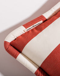 Close-up of the Small Square Throw Pillow - Crew Le Sirenuse Stripe by Business & Pleasure Co, featuring red and white stripes and a sewn-in “leisure & pleasure” label, angled on a white background—ideal for indoor-outdoor pillow collections.