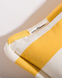 Close-up of the Small Square Throw Pillow - Crew Mimosa Yellow Stripe by Business & Pleasure Co., featuring a fabric tag and crafted with Pleasuretex fabric. The cushion is well-lit and shows soft shadows for an inviting look.