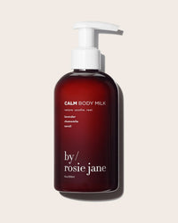 A dark amber pump bottle labeled Calm Body Milk by Rosie Jane, featuring lavender, chamomile, and neroli, stands against a plain light background.