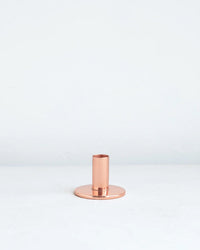 The Floral Society’s Copper Taper Holder - Medium features a minimalistic, handmade design with a cylindrical base, displayed on a plain white surface against a light background.