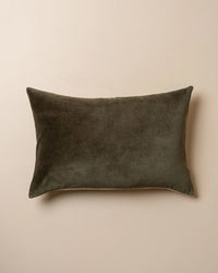 The Saarde Velvet Lumbar Pillow with Feather Insert in Dark Olive rests on a plain beige surface.
