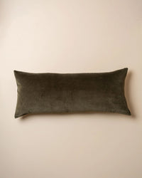 The Saarde Velvet Body Pillow w/ Feather Insert in Dark Olive rests on a plain beige surface.