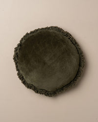 The Saarde Velvet Round Pillow w/ Feather Insert in Dark Olive features a fringed edge and round shape, shown against a plain light background.