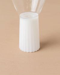 Close-up of the base of the Saarde Kairos Wine Glass in Opaque White, featuring a ribbed cylindrical stand, set on a light beige surface.