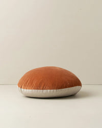The Saarde Linen/Velvet Round Pillow w/ Feather Insert in Terracotta features a rust-toned top and light beige bottom, displayed against a plain off-white background.