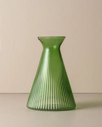 The Saarde Kairos Angular Carafe in Green, featuring a ribbed conical design and crafted from borosilicate glass, is set against a plain beige background.