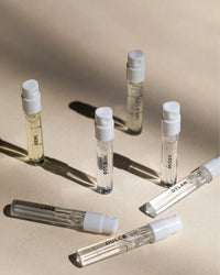 Six small sample vials with white caps from the Rosie Jane Fragrance Discovery Set are arranged on a beige surface, each labeled with REMI, ROSIE, MISSY, DULCE, LAKE, or HELA LOU.