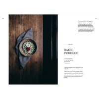 A rustic wooden table holds a bowl of baked porridge with red berries and seeds on a gray cloth. On the right, Cozy Publishing's "Four Seasons of Cabin Cooking" features its baked porridge recipe in black text on white.