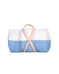 The Suave Aire - Blanket Roll by caminito is a handwoven indoor/outdoor blanket in blue, white, and beige, secured with a tan leather strap and handy handle. Displayed against a white background.