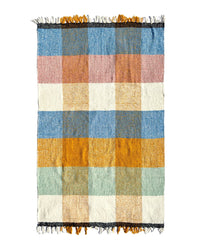 The Suave Campo - Blanket Roll by caminito is a handwoven rectangular indoor/outdoor blanket from Mexico, featuring a large blue, mustard yellow, off-white, light green, and dusty pink checkered pattern with fringed short edges.