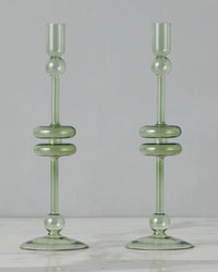 The etúHOME Sage Glass Candlesticks Set of 2 - Large, crafted from recycled glass in translucent green with round and disc accents, stand side by side on a white marble surface.