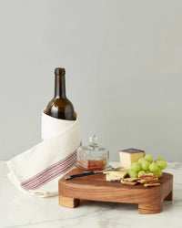 A wine bottle in a white towel, cheese, crackers, green grapes, and the etúHOME Bistro Glass Jam Jar, Square, are arranged on a wooden board atop a marble surface.