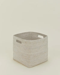 The Hawkins New York Essential Woven Storage - Square Basket in light beige seagrass features two rectangular cutout handles and is shown on a plain, off-white background.