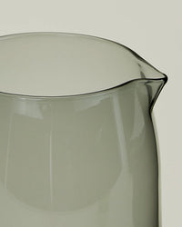 Close-up of the Hawkins New York Essential Glassware - Pitcher in Smoke, a 52 oz transparent grey-tinted pitcher with a subtle spout, set against a plain light background.