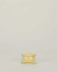 A Simple Glass Butter Keeper from Hawkins New York, filled with pale yellow butter, sits on a plain, light-colored background with ample empty space above.