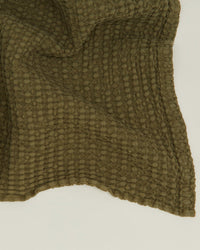Close-up of the Hawkins New York Simple Waffle Bath Sheet in Olive, a textured Portuguese-made towel with a waffle weave pattern, shown slightly wrinkled against a plain light background.