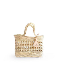 The Canasta Mini Bag in Natural by caminito is a small woven palm purse with two handles and a tan leather tag, crafted from natural straw and shown on a plain white background.