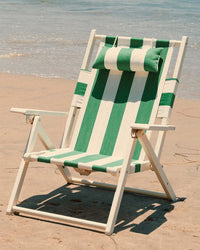 The Tommy Chair - Acacia White - Crew Canyon Green Stripe by Business & Pleasure Co sits empty on the sand, its green and white stripes and comfortable sling ready for relaxation by the waves.