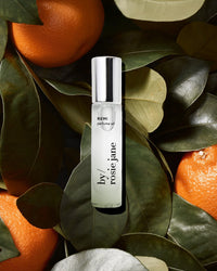 A bottle of Rosie Jane Perfume Oil in Remi sits on green leaves among fresh oranges, evoking the bright, citrusy scent of California.