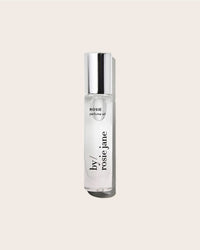 The Perfume Oil in Rosie by Rosie Jane is a clear glass bottle with a silver cap, shown against a beige background. This fragrance offers a delicate skin scent with soft notes of white musk.