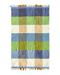 The Suave Kiwi - Blanket Roll by caminito is an ultra-soft, handwoven Mexican throw with a large blue, green, yellow, and white checkered pattern plus white/yellow fringe—perfect for indoor or outdoor use.