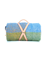 The Suave Kiwi - Blanket Roll by caminito is a handwoven, ultra-soft throw in blue, green, and yellow hues, rolled up and secured with a tan leather strap and handle, shown on a white background.