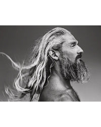 Surf Tribe by Simon & Schuster: A black-and-white portrait captures a bearded man in profile, his long wavy hair flowing behind him, evoking surf culture’s raw spirit. Minimal background and lighting highlight the texture of his hair and beard.