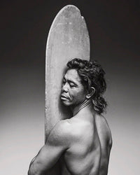 In this striking black-and-white portrait from "Surf Tribe" by Simon & Schuster, a long-haired, shirtless person rests with closed eyes against a surfboard, reflecting the tranquil spirit of surf culture.