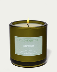 A lit Flamingo Estate Coriandoli Candle, 8 oz hand-poured vegetable wax in a green glass jar with branded label, shown against a plain white background.
