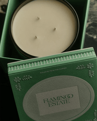 A green box holds Flamingo Estate’s The Tomato XL Candle, crafted from vegetable wax, beside its matching lid embossed with decorative patterns and the phrase Pleasure from the Garden.
