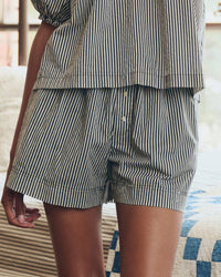 A person indoors wears the Great. Sleep's The Sleep Boxer Short in Black & Cream Crew Stripe and a matching short-sleeved shirt. The shorts have an elastic waistband, are made from 100% cotton, and only the torso and upper legs are visible.