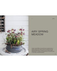 The Potted Garden - All Year Round by Cozy Publishing features striking snake’s head fritillary flowers with purple chequered petals and green leaves, arranged on a white surface beside pinecones and a branch against a white plank wall.