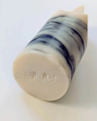 A cylindrical Erode Soap Mini in Jasmine Ylang Ylang by Ume Studio, featuring dark and light marbled swirls, lies on its side with UUU stamped on one flat end.